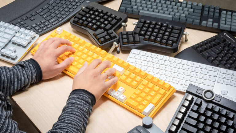 multiple keyboards on a desk and someone typing on one of them