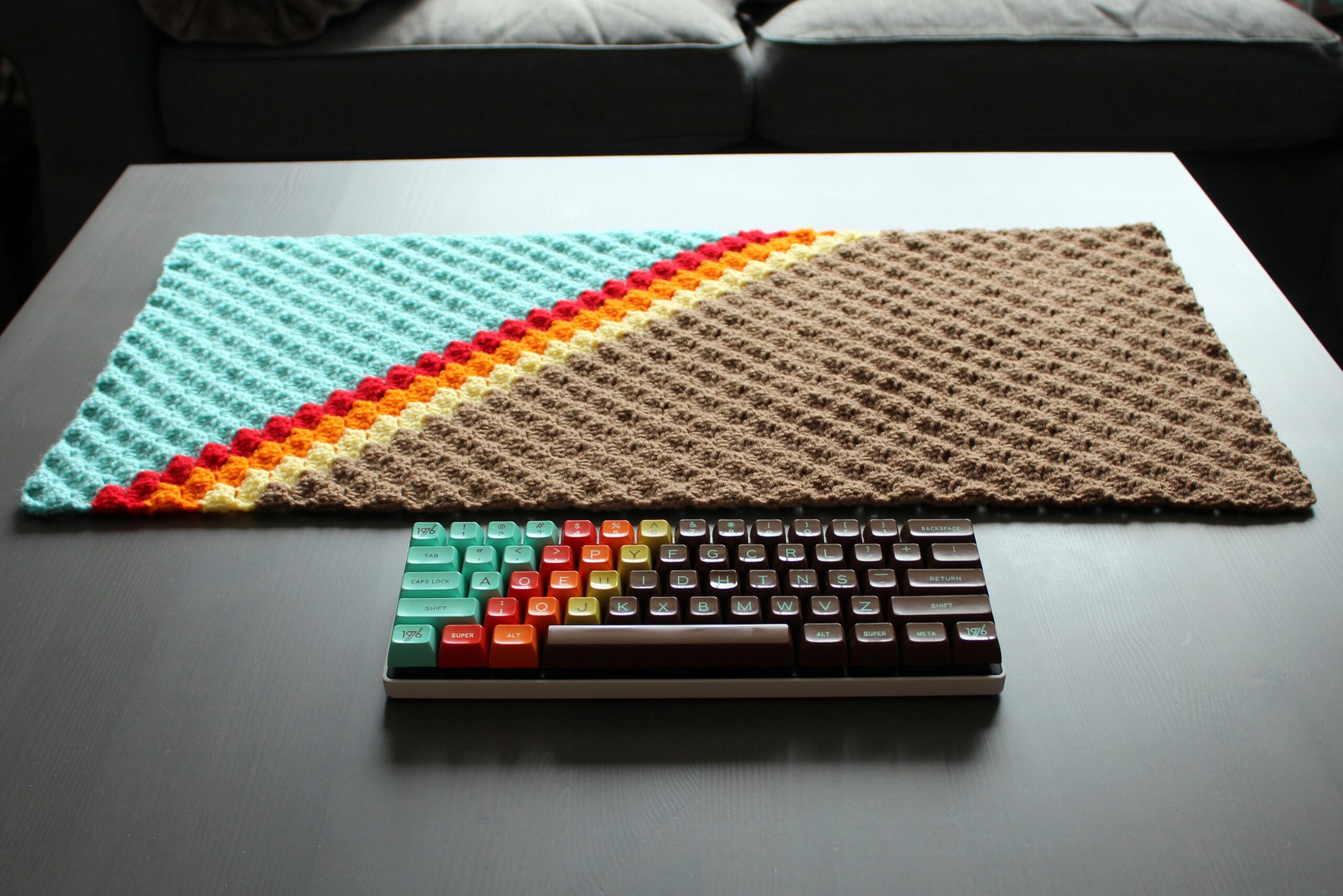 Teal and brown gradient keycaps keyboard on a table with a matching crochet pad